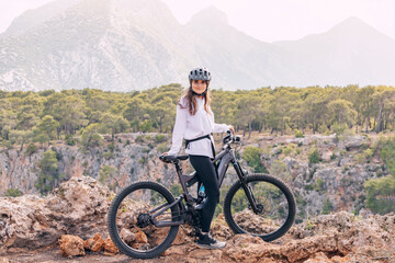 Happy girl wearing helmet and sportswear with her hightech electric bicycle on top of a canyon