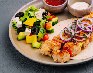 chicken skewers with greek salad and creamy, spicy sauces