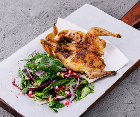 Roasted grilled quail on wooden cutting board with garnish green salad
