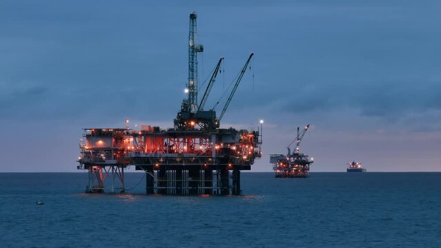 Beautiful aerial view of the offshore oil drilling rig, remaining afloat on the open ocean and illuminated ships, floating aside. Oil and gas extraction. High quality 4k footage
