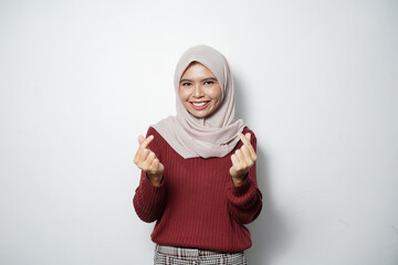 Beautiful smiling Asian woman in red sweater showing Korean heart with two fingers crossed, express joy and positivity isolated over white background