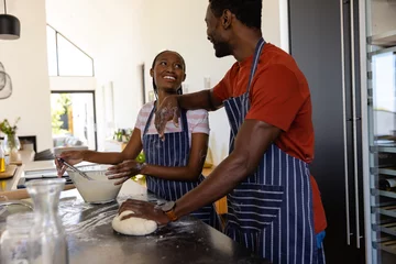 Gordijnen Happy african american couple in aprons preparing bread dough in kitchen © WavebreakMediaMicro