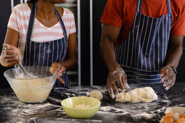 Mid section of african american couple in aprons preparing bread dough in kitchen - Powered by Adobe
