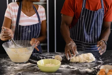 Gordijnen Mid section of african american couple in aprons preparing bread dough in kitchen © wavebreak3