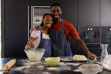 Tuinposter Portrait of happy african american couple in aprons preparing bread dough in kitchen © WavebreakMediaMicro