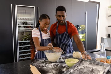 Zelfklevend Fotobehang Happy african american couple in aprons preparing bread dough in kitchen © wavebreak3