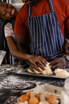 Happy african american couple in aprons preparing bread dough in kitchen