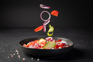 Delicious fresh salad with tomatoes, cucumber, onion and cheese on dark background. Flying...