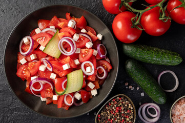 Delicious fresh salad with tomatoes, cucumber, onion and cheese on dark background, top view. Salata de rosii cu castraveti, ceapa si branza.