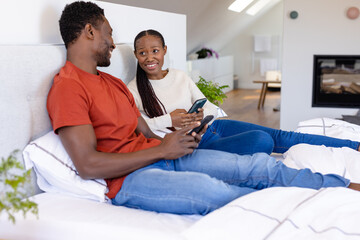 Happy african american couple using smartphones lying on bed in bedroom