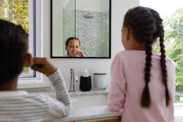 Biracial brother and sister in pyjamas brushing teeth together in the morning in bathroom