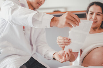 Obraz premium Concept Motherhood and Pregnant, Prenatal care and pregnancy. Male doctor showing ultrasound picture to pregnant woman with pregnant woman in hospital.