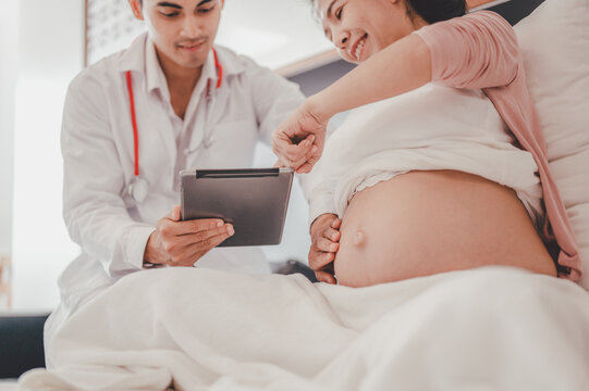 Concept Motherhood and Pregnant, Prenatal care and pregnancy. Male doctor showing digital tablet with baby ultrasound picture on tablet to pregnant woman sitting on the bed.