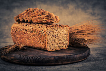 Sliced rye bread on wooden board and ears of wheat on gray background