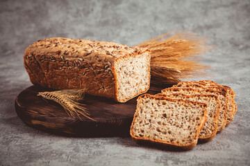 Sliced rye bread on wooden board and ears of wheat on gray background