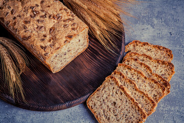 Sliced rye bread on wooden board and ears of wheat on gray background