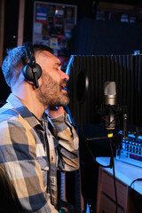 Male singer wearing headphones performing a new single with a microphone, recording it in a music...