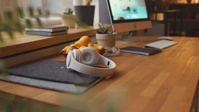 No people shot of modern wireless headphones on wooden desk by window in cozy studio apartment with warm light