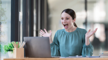 Overjoyed surprised woman looking at laptop screen, sitting at a work desk, reading good unexpected...
