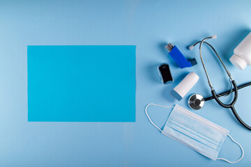 Medical mask, stethoscope, oximeter, bottle of pills and inhalers on light blue background with vibrant blue rectangular sheet of paper for text placement. Asthmatic breathing symptoms Concept - obrazy, fototapety, plakaty