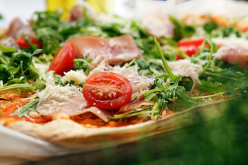 Italian pizza with cherry tomato, Italian ham, cheese and arugula, close-up, selective focus.
