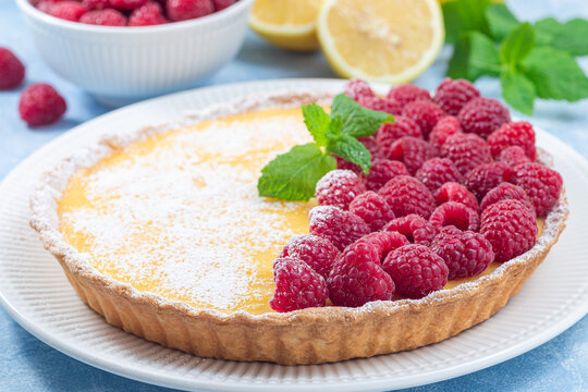 Lemon tart, garnished with fresh raspberry, icing sugar, mint, horizontal
