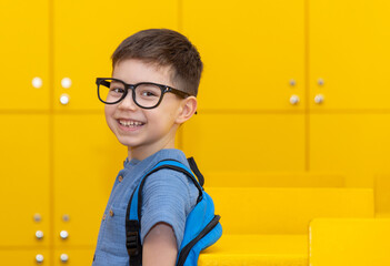 back to school happy preschooler boy kid in classroom happy smiling face or bored expression sitting at table.boy with glasses frame on eyes or magnifying glass.child carrying many books,backpack - obrazy, fototapety, plakaty