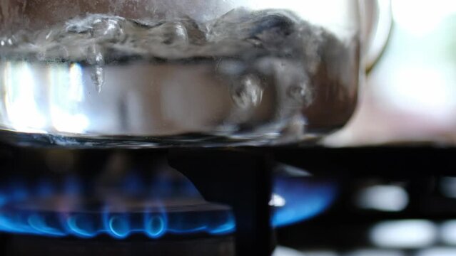 Close up shot of a glass kettle of water boils. Blue flame .