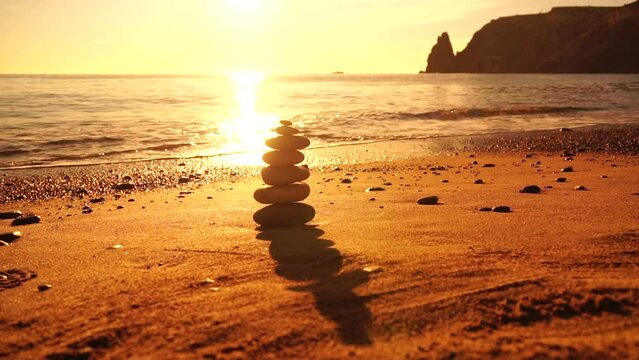 Balanced rock pyramid on pebbles beach, sunny day and clear sky at sunset. Golden sea bokeh on background. Selective focus, zen stones on sea beach, meditation, spa, harmony, calm, balance concept.