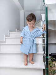 Fototapeta na wymiar cute boy baby toddler kid in bathrobe in modern bathroom interior in front of sink.product clothes photo, smiling child in shower.different colors bathrobe on hangers.towel with hood