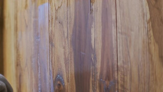 Hand in glove holding brush is applying lacquer or protective varnish on wooden wall. Protect the wood from moisture.