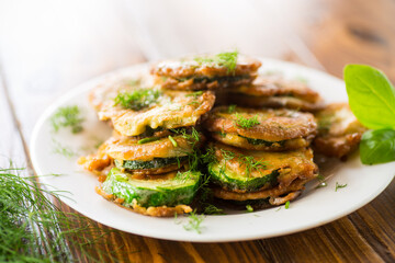 zucchini fried in circles in batter with herbs, in a plate .