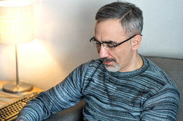 Adult middle aged man. He is wearing a casual sweater. Face with gray beard and thick eyebrows. Chest-length lifestyle portrait of matured caucasian person