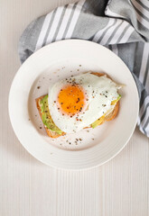 Toast with avocado on a white plate, made from whole grain bread, fried egg top view with a copy of the space