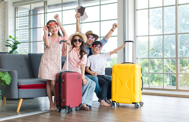 Asian cheerful happy family mom dad son and daughter wearing sunglasses and hat with two trolley luggages raising hands smiling celebrating holiday together ready for traveling vacation road trip