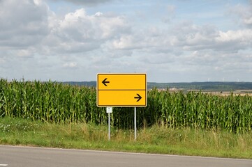 Yellow direction street sign pointing down a winding country road