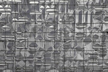 Closeup of a glass mosaic wall with a metallic sheet covering it in a grey and silver color