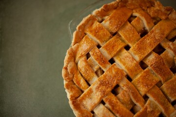 Delicious homemade peach pie with decorative lattice crust and a sprinkle of sugar on a green table
