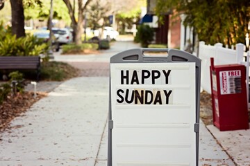 Street sign with the words 'Happy Sunday' written on it, placed on the side of the road
