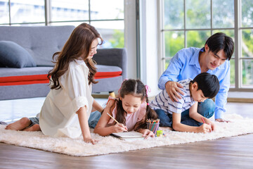 Asian happy cheerful joyful family husband and wife lover couple sitting on carpet floor helping teaching little boy son and girl daughter painting drawing cartoon with color pencils in living room