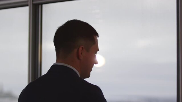 Businessman ready for phone call with close person near office window side view. Young man enjoys mobile phone conversation