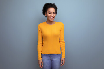 pretty 20s latin woman with afro hair in casual yellow blouse posing on studio background