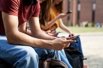 Fototapeta na wymiar Unrecognizable university students browsing phones next to university campus building