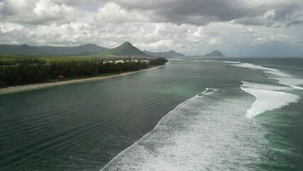 Drone view above sea waves covering a forested coastline