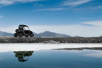 Utility Task Vehicle (UTV) cruising along the water near the majestic mountain range in background