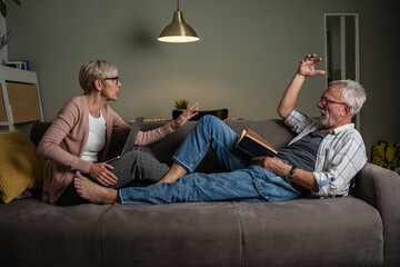 Senior couple sitting on sofa and arguing about something.	

