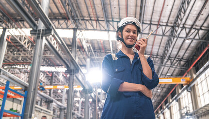 Female engineer in uniform and safety helmet holding walkie talkie talking to electric train repairman at electric train depot
