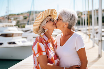 Senior gay lesbian couple kissing outside - LGBTQ aged tourists having tender moment during summer vacation. Generative AI - obrazy, fototapety, plakaty
