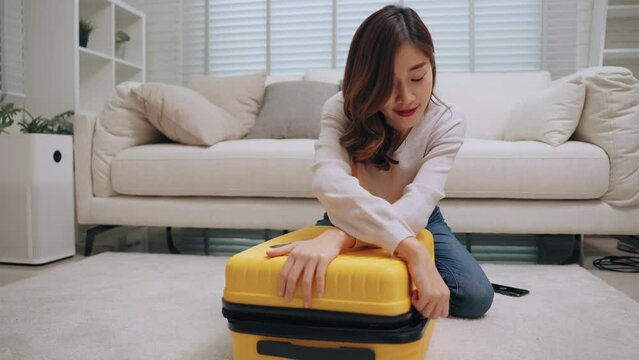 Young asian woman packing clothes and close the zipper yellow luggage in living room before the trip of long weekend holiday. Traveling and long weekend concept