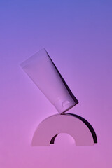 white cosmetic tube on a pink neon background on white podium. The concept of a cream